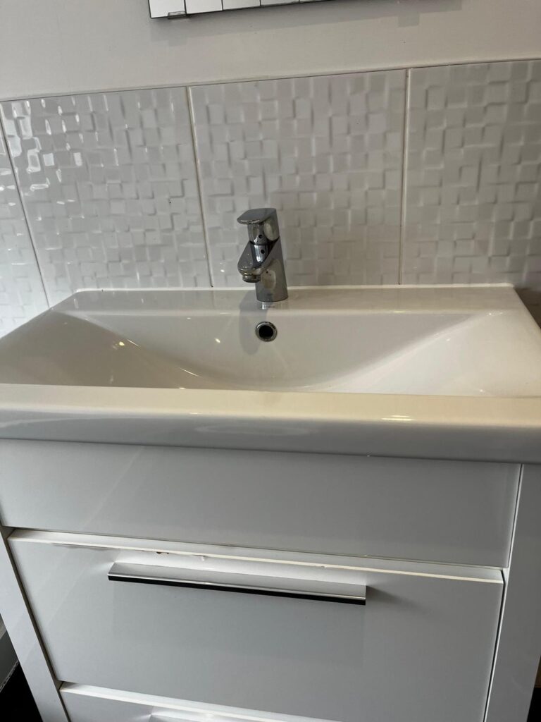 Modern white bathroom sink and chrome tap after a professional deep clean, with polished surfaces and clean wall tiles.